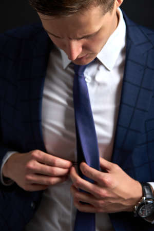 unrecognizable male straighten tie on suit, handsome guy looks down on tie, isolatedの写真素材