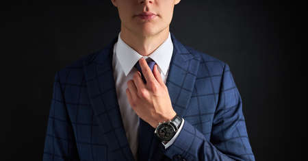 cropped business man straighten a tie isolated over black background. young guy in formal suit preparing for meetingの写真素材