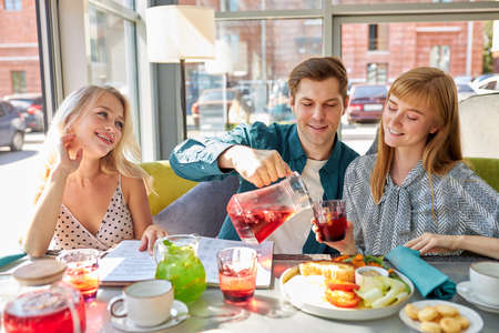 happy caucasian friends are resting in cafe having meal and fun, they are sitting at a table, talk and share newsの写真素材