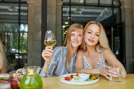 portrait of good-looking smiling caucasian women in restaurant, they sit together, hold glass of champagne in hands and look at cameraの写真素材
