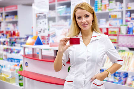 portrait of good-looking drugstore worker holding props card of pharmacy in hands, pleasant affable druggist welcomes clients and customersの写真素材