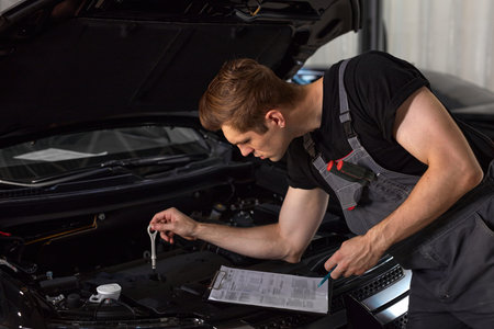 handsome caucasian guy is making notes while repairing hood of car, check all missing attributes...