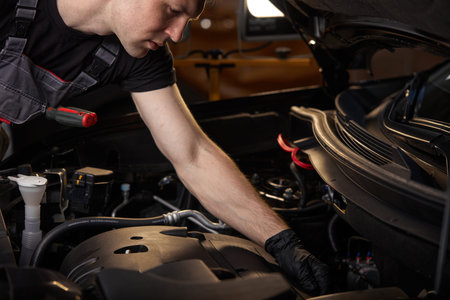 young caucasian professional auto mechanic in a car service, checks a car, engine, carburetor. car...
