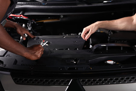 close-up photo of two unrecognizable auto service workers immersed in work, repairing car hood