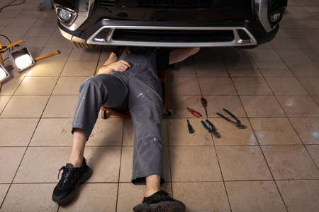 unrecognizable auto mechanic lying and working under car, top view. necessary instruments on the floor next to himの写真素材