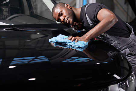 black man holds the microfiber in hand and polishes the car in auto service, do it carefully after repairの写真素材