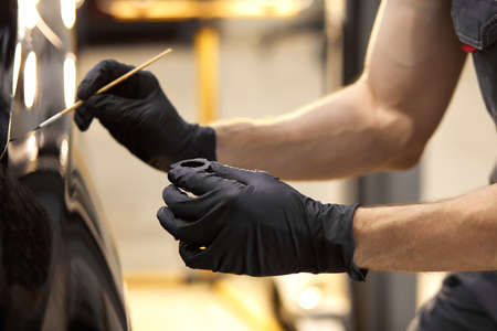 confident auto mechanic man using brush for painting a car, applying paint of black representative automobile after scratchingの写真素材