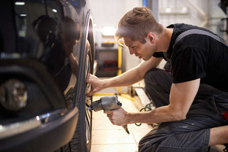 concentrated professional auto mechanic man repairs a wheel that has broken, changingの写真素材