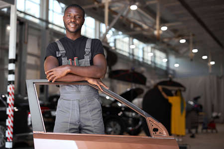 young african auto mechanic at work with separate part of the machine, posing at camera, going to repairの写真素材