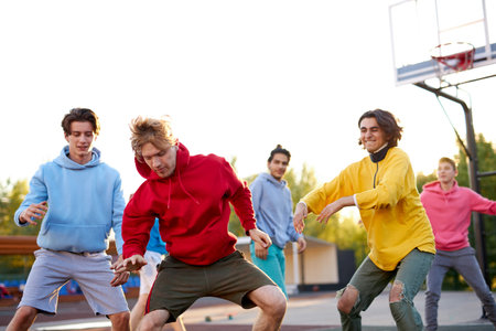 group of young male teenagers in colourful hoodies playing basketball outdoors in the street