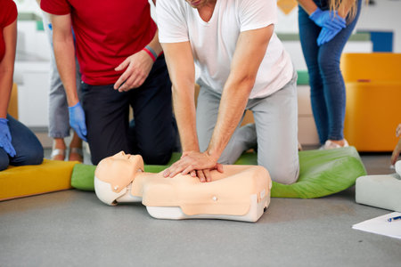 young male practicing CPR first aid on a mannequin in the presence of people, indoors