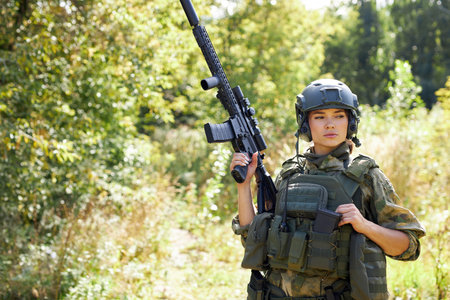 portrait of confident military woman with a gun in forest, hunter female in camouflage suit with a...