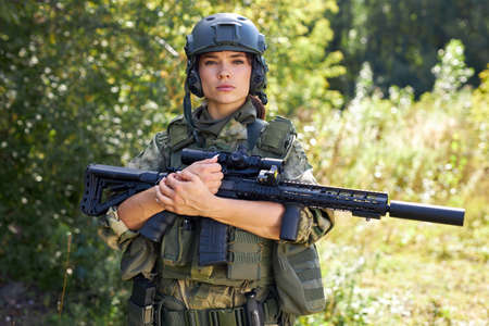 portrait of confident military woman with a gun in forest, hunter female in camouflage suit with a gun stand in nature aloneの写真素材
