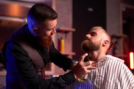 caucasian hipster client man visiting in barber shop shaving beard by professional hairdresser, stylish and and modern beard in salonの写真素材