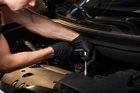young caucasian professional auto mechanic in a car service, checks a car, engine, carburetor. car...