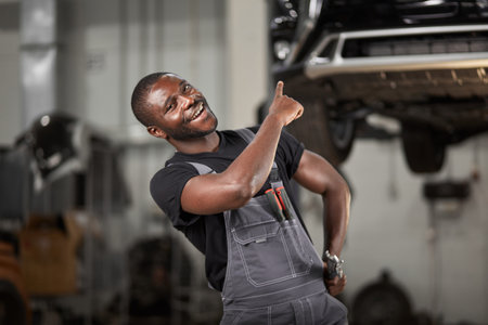 portrait of positive afro american auto mechanic in uniform posing after work, he is keen on repairing cars, automobiles.の写真素材