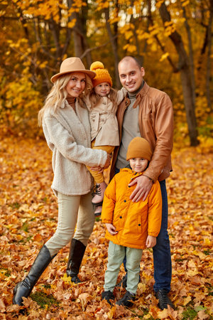 full-length portrait of young family with children posing at camera, attractive parents with kids look at camera in autumn parkの写真素材