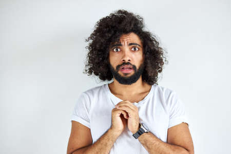 scared curly arabian young guy stand in fear by something, look at camera, isolated over white background.の写真素材