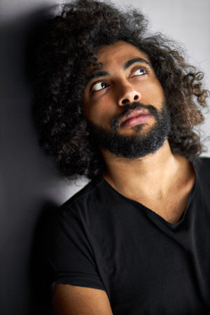 dreamy curly arabian male looking up, bearded guy is thinking about something , isolated black...