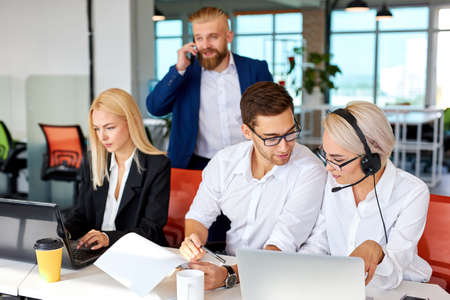 young team concentrated on work on laptop while director near them , sit at table together, successful cooperation. male boss checking the work processの写真素材