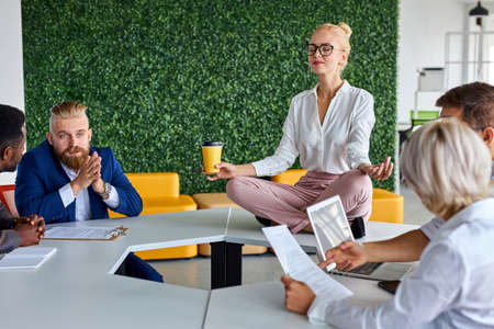 young caucasian woman meditating in office while colleagues are working, keep calm, meditate. sits on table with crossed legsの写真素材