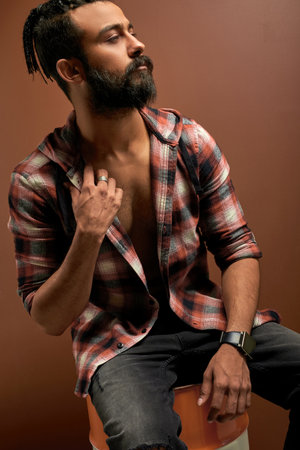 half-naked arab indian guy in casual shirt posing in studio with brown background, handsome fashionable male looking at side, model. style, fashion, people concept.の写真素材
