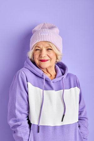mature woman in purple pullover and hat posing, stylish woman enjoy being fashionable, looks at cameraの写真素材