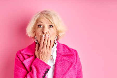 scared and shocked senior woman close mouth, emotionally react on something isolated over pink backgroundの写真素材