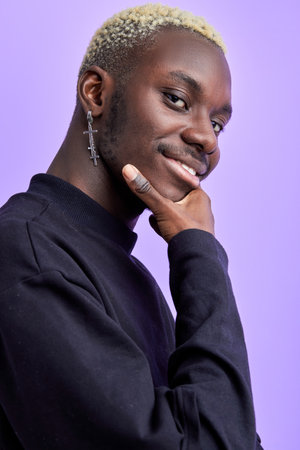 black guy in casual black wear looks at camera touching the chin, smiling isolated over purple backgroundの写真素材