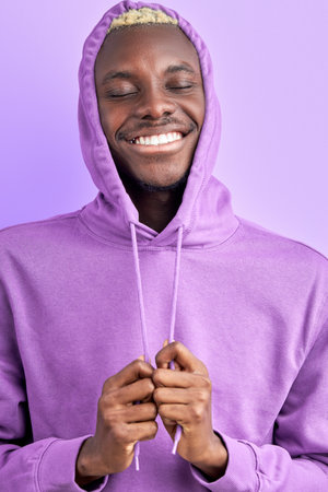 black male model in purple pullover posing at camera isolated in studio, smiling with closed eyesの写真素材