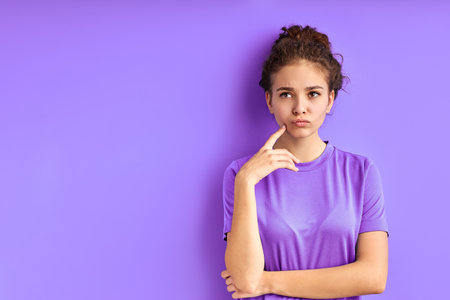 young upset girl is thinking about something sad, stand looking away, isolated over purple backgroundの写真素材