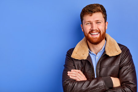 cool trendy male in winter or autumn coat posing at camera standing with crossed arms, smiling