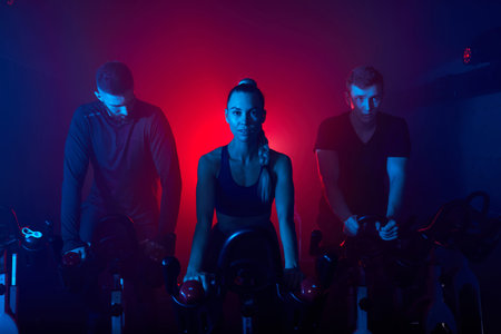 people working out on the exercise bike at the gym, intense cardio workout. men and women in...
