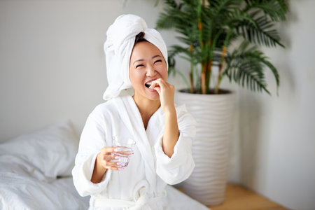 female taking pills and a glass of water for treatment, in the morning. nice woman drinks vitamins for disease prevention. wellness and health conceptの写真素材