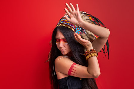 woman in creative shaman makeup making rituals, shamaning with arms, dancing, wearing traditional ethnic plume roach feathersの写真素材