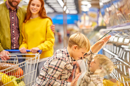 kid boy leaned on showcase in supermarket while parents shopping together, wants parents to buy something he dreamed about.の写真素材