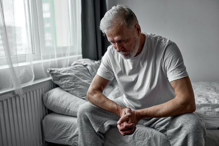 depressed senior man sits thoughtful looking down, melancholic male alone at homeの写真素材