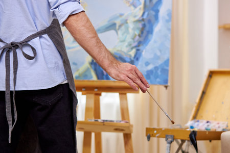 male painter in apron making masterpiece with brush on canvas, picture on easel. design, art, craft, painting conceptの写真素材