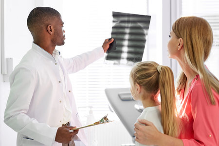 black male pediatrician explaining and showing lug x-ray for sick child and mother in hospital...