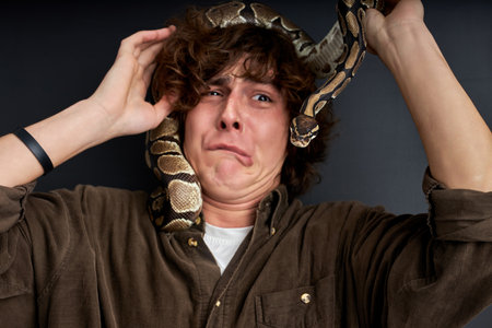 man has a panic, he is trying to remove a live snake from himself, stand at a loss isolated on black backgroundの写真素材
