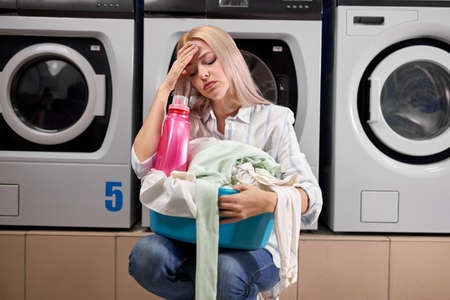 woman doing laundry, looking sad and depressed expression, having bad mood after hard working day, in washing house. tired and exhausted staffの写真素材