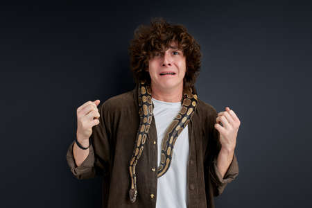 man trying to keep calm while exotic snake is crawling on him, isolated over black backgroundの写真素材