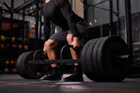 cropped bodybuilder guy prepare to do exercises with barbell in dark modern fitness center or gym.bodybuilders hand is liftingbarbell and exercising, alone, man dressed in sportive clothes. side viewの写真素材