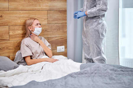 woman has respiratory symptoms fever, coughing, body aches sitting on bed at home talking with...
