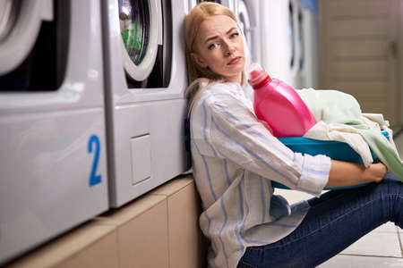woman doing laundry, looking sad and depressed expression, having bad mood after hard working day, in washing house. tired and exhausted staffの写真素材
