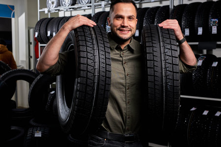 client guy stands with two tires by rack of tires, he made choice, buy the best ones in auto service...