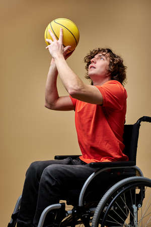 man on wheelchair is playing a ball to strengthen muscles, holding yellow basketball ball. lifestyle of disability people, isolated beige backgroundの写真素材