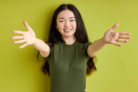 lets hug you. young caucasian woman spreading arms going to hug everyone, expressing thanks and love, smiling at camera. isolated green backgroundの写真素材
