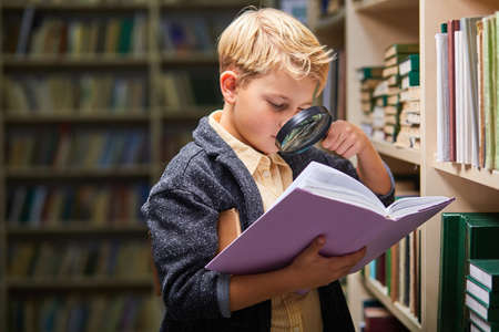 school little boy using magnifying glass for reading, get new information for brain in libraryの写真素材