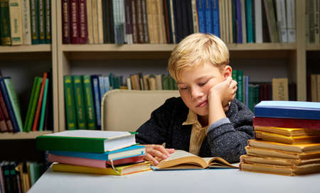 sleepy boy sitting at table with books in library. tired to study. Education, Knowledge, Bookstore, Lecture conceptの写真素材